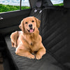 A golden retriever sits in a black car seat cover with armrest access inside a vehicle.