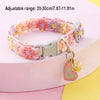Pink and purple adjustable lace pet collar with a gold heart pendant displayed on a pink surface.
