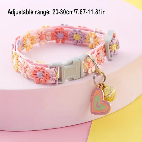 Pink and purple adjustable lace pet collar with a gold heart pendant displayed on a pink surface.