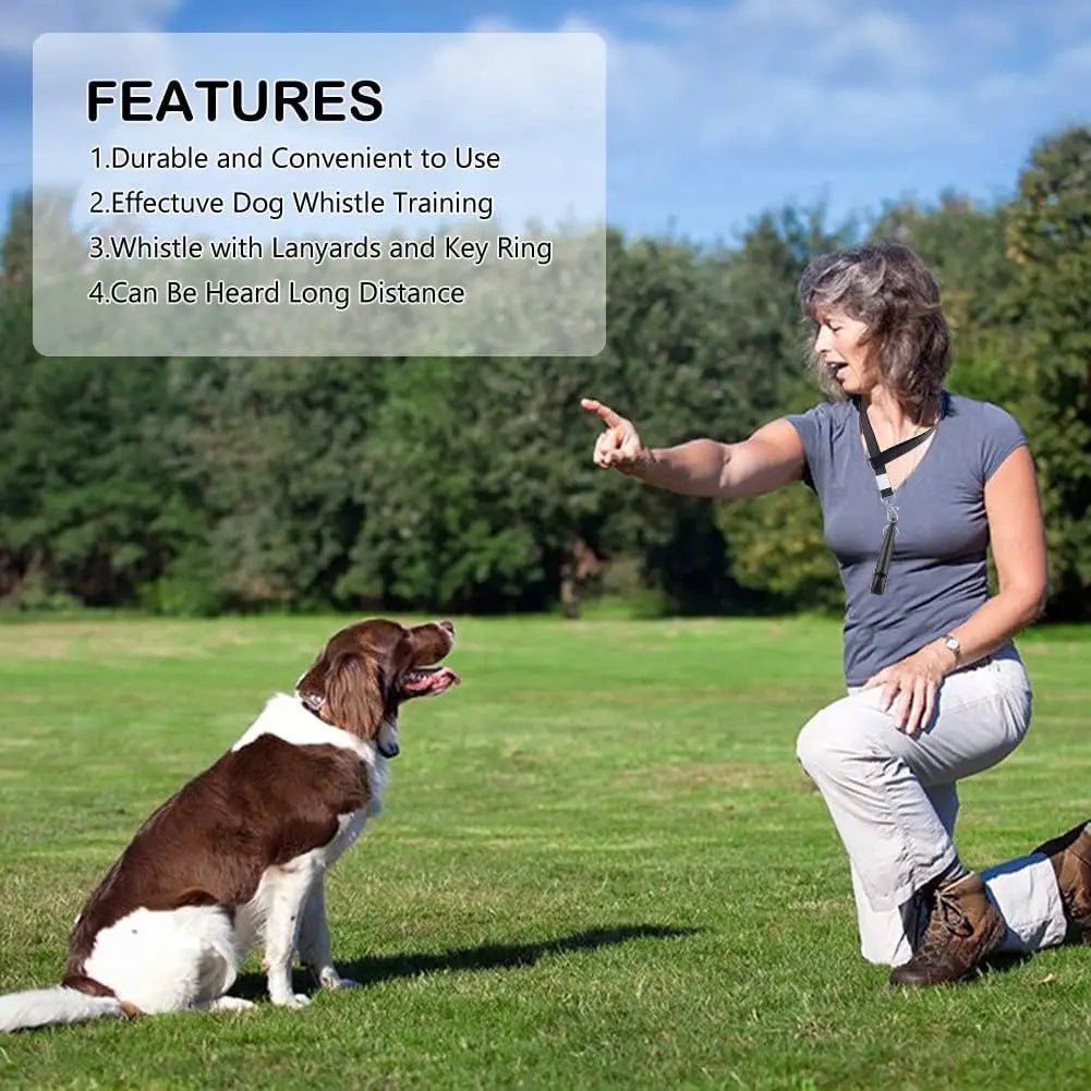 A woman is demonstrating an ultrasonic dog whistle to a dog in a grassy outdoor setting.