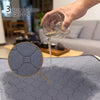 A hand pours liquid from a glass onto a gray, hexagonal fleece liner for small pets.