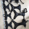 A set of black adjustable no-pull dog harnesses with reflective strips and handles laid out on a light surface.