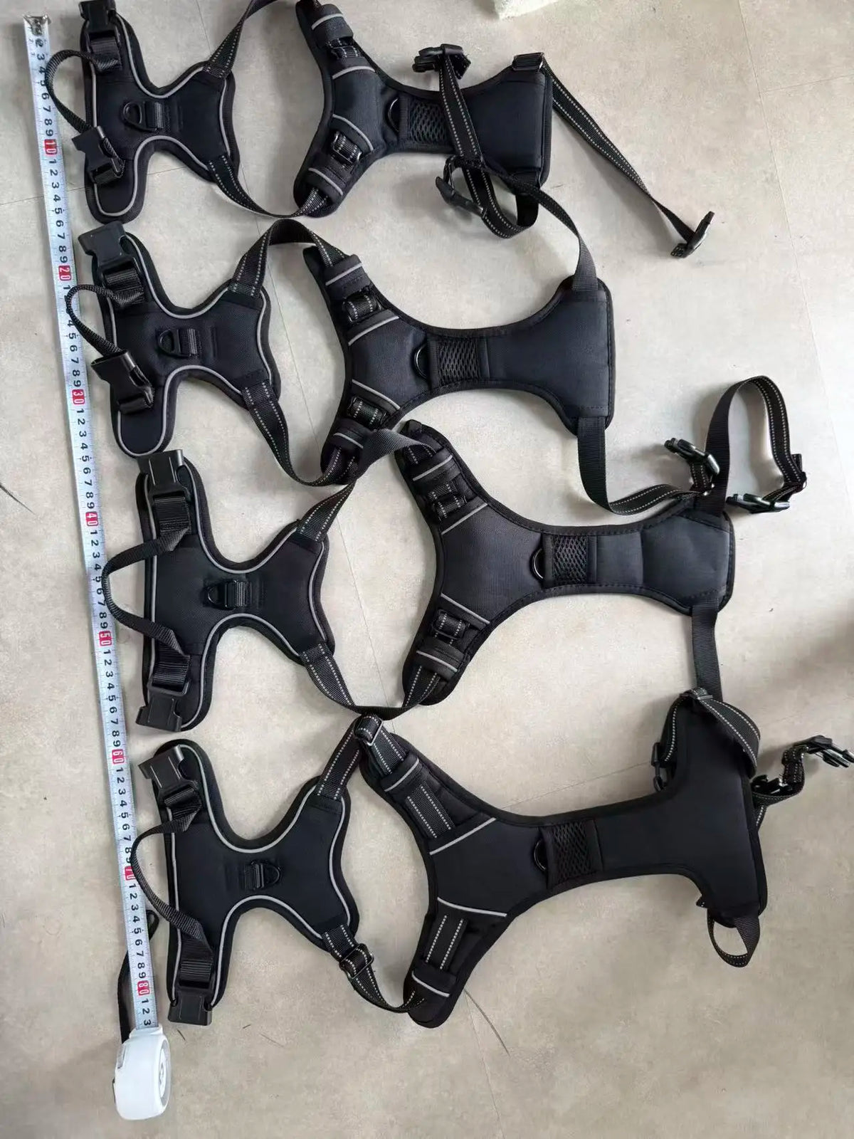 A set of black adjustable no-pull dog harnesses with reflective strips and handles laid out on a light surface.