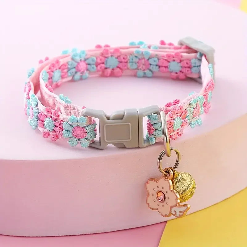 Pink and blue lace pet collar with a gold pendant resting on a pink surface.