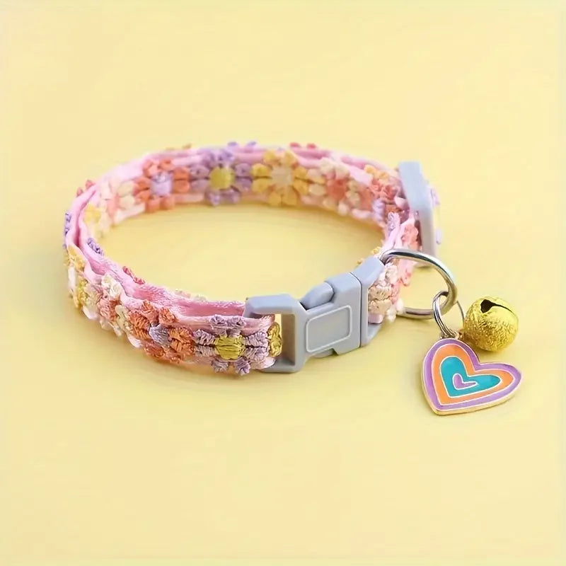 A pink and purple lace pet collar with a heart-shaped pendant is displayed on a light yellow background.