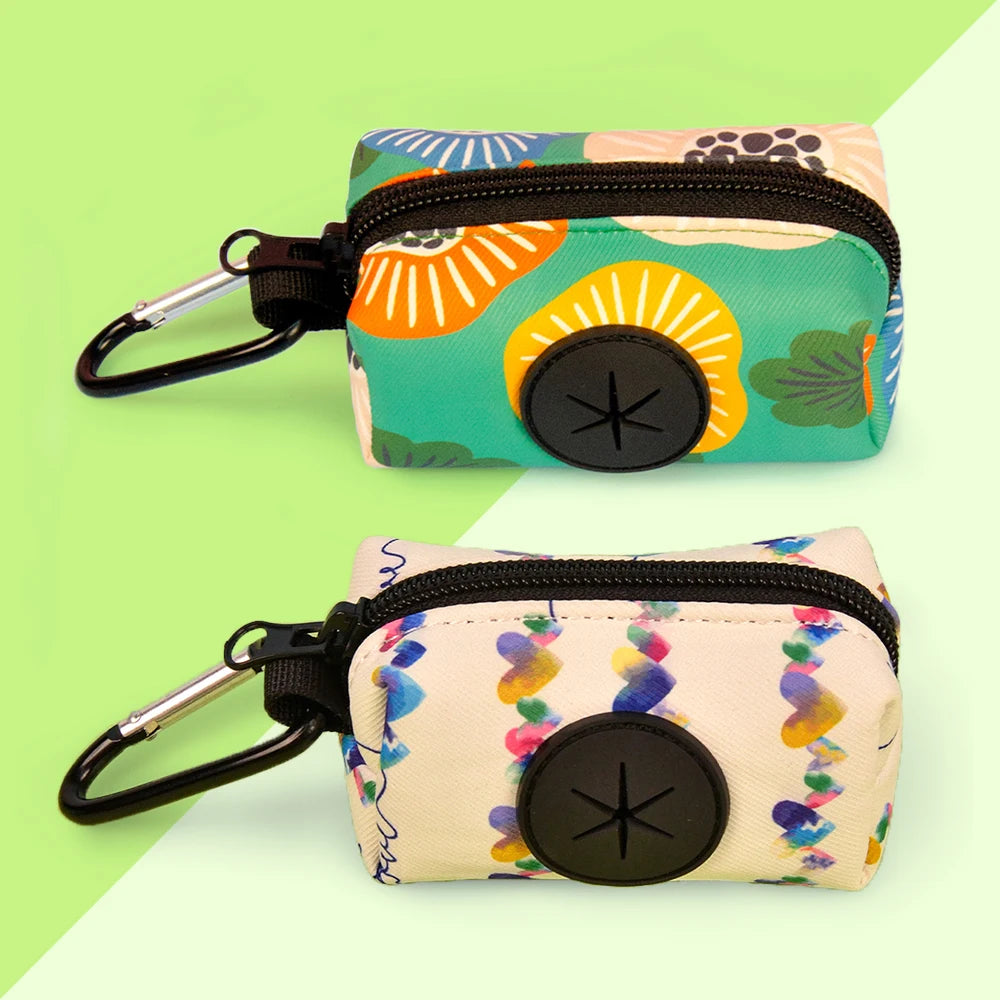 A pair of colorful fabric poop bag holders with black zippers and metal clasps are shown against a light green background.
