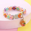 A colorful adjustable lace pet collar with a floral pattern and a gold pendant displayed on a pink surface.