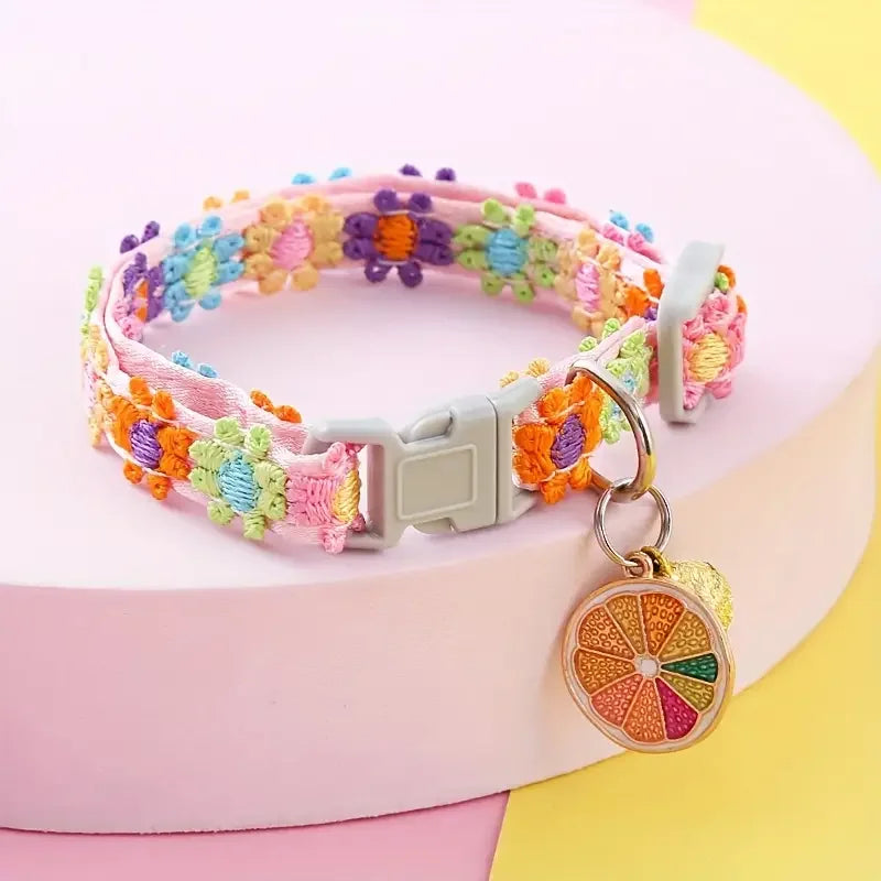 A colorful adjustable lace pet collar with a floral pattern and a gold pendant displayed on a pink surface.