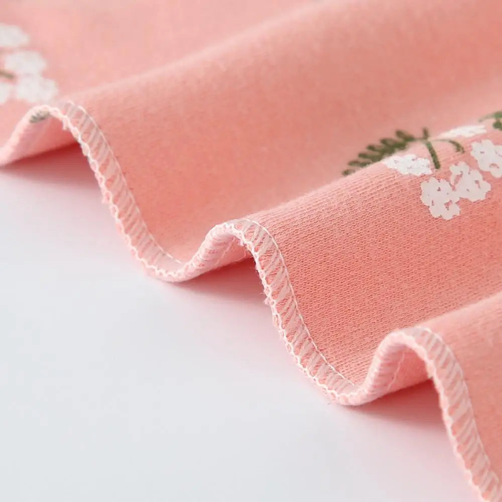 A pink cotton bandana with a white floral print folded and displayed on a white background.