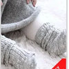 Graue Strickbaby-Socken mit Cartoon-Tierdesign auf weißem flauschigem Fell.