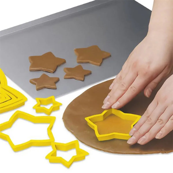 A hand is using yellow star-shaped cookie cutters to cut dough, with several brown star-shaped cutouts visible on a gray sili