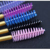 A collection of disposable eyelash brushes in various shades of purple, blue, and black laid out on a dark surface.