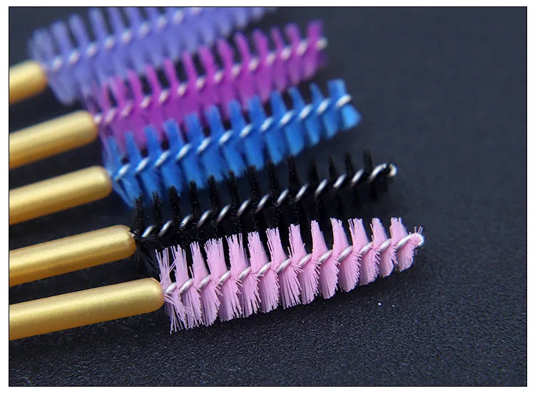 A collection of disposable eyelash brushes in various shades of purple, blue, and black laid out on a dark surface.
