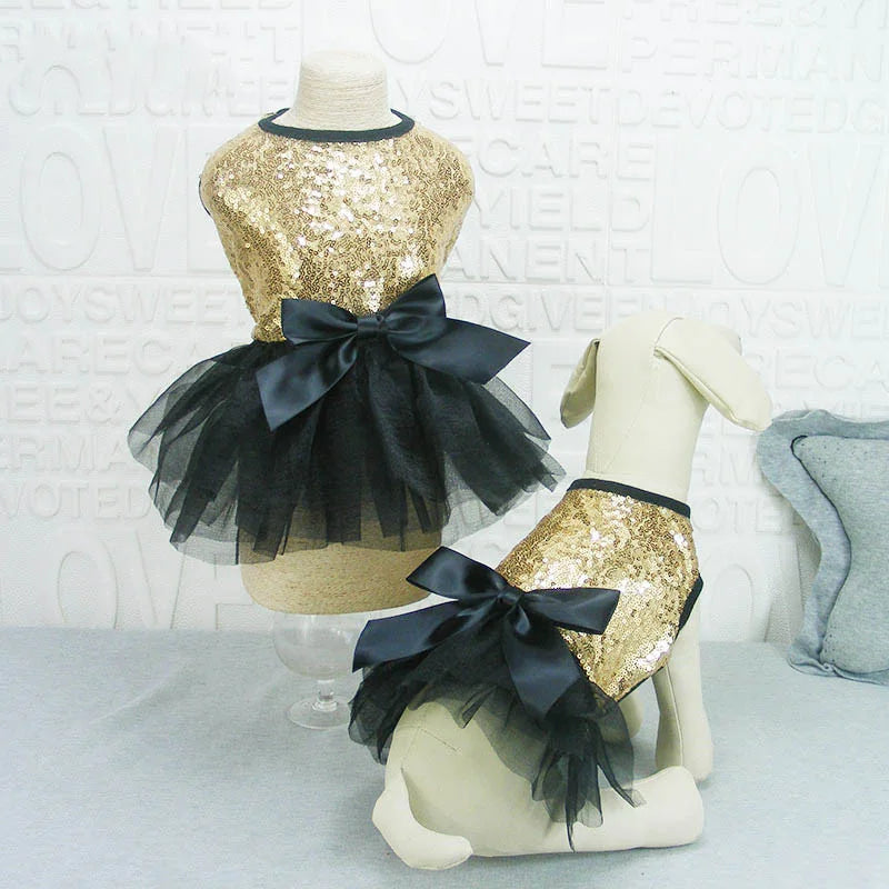 A gold sequined dog dress with a black bow and tulle skirt displayed on a mannequin.