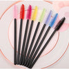 A collection of various colored disposable eyelash brushes arranged on a pink plate.