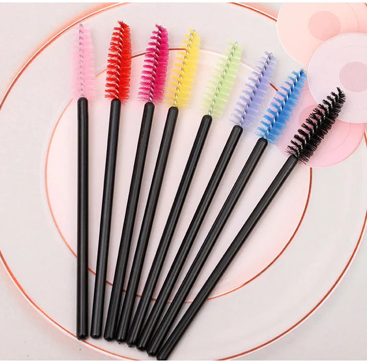 A collection of various colored disposable eyelash brushes arranged on a pink plate.