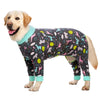 A golden retriever wearing a dark jumpsuit with a colorful cartoon animal print and light blue trim.