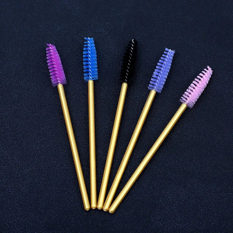 Five disposable eyelash brushes in purple, blue, black, and pink are arranged diagonally on a dark surface.