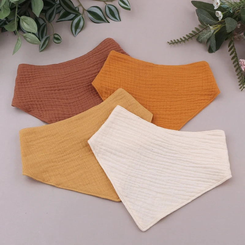 A set of three soft cotton baby bibs in shades of terracotta, orange, and cream laid on a neutral background.