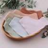 A woven basket holds three soft cotton baby bibs in shades of beige, pink, and sage green.