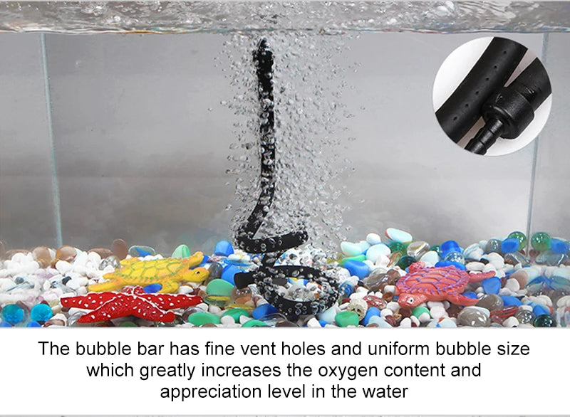 A black tube aerator is shown spraying bubbles into a fish tank filled with colorful aquarium gravel and fish.