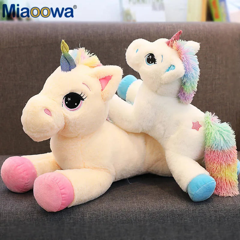 A white unicorn plush toy with rainbow colored mane and hooves sitting on a dark gray surface.