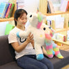 A young woman is holding a white unicorn plush toy with pink and rainbow accents in a bright indoor setting.