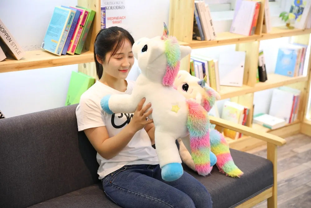 A young woman is holding a white unicorn plush toy with pink and rainbow accents in a bright indoor setting.