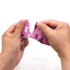 Hands are applying a pink and black patterned self-adhesive elastic bandage tape to a finger.