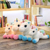 A set of five white unicorn plush toys with colorful manes and pink feet sitting on a wooden floor.