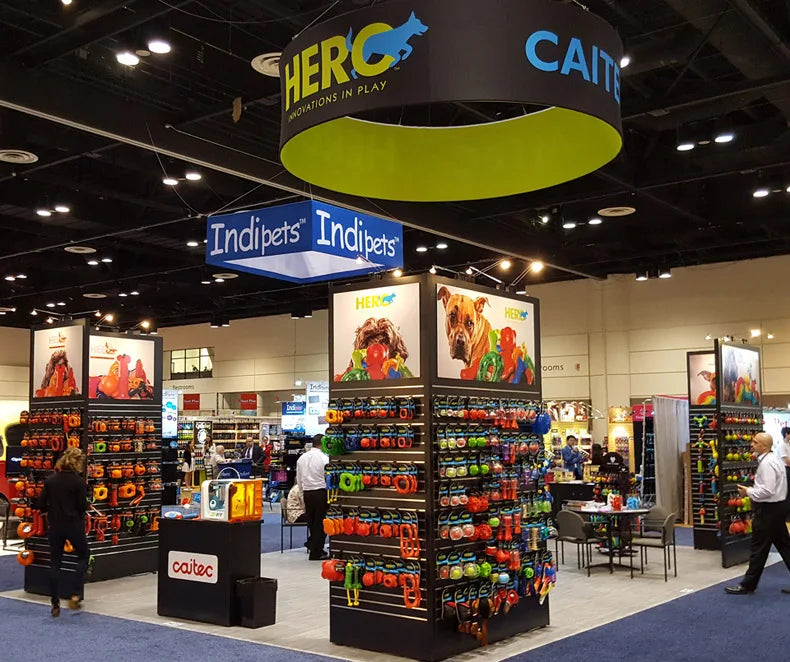 Exhibición de juguetes para perros squeaky y saltarines Hero Indipets y productos relacionados en un stand de feria.