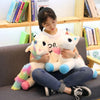 A young woman is sitting on a couch holding two white unicorn plush toys.