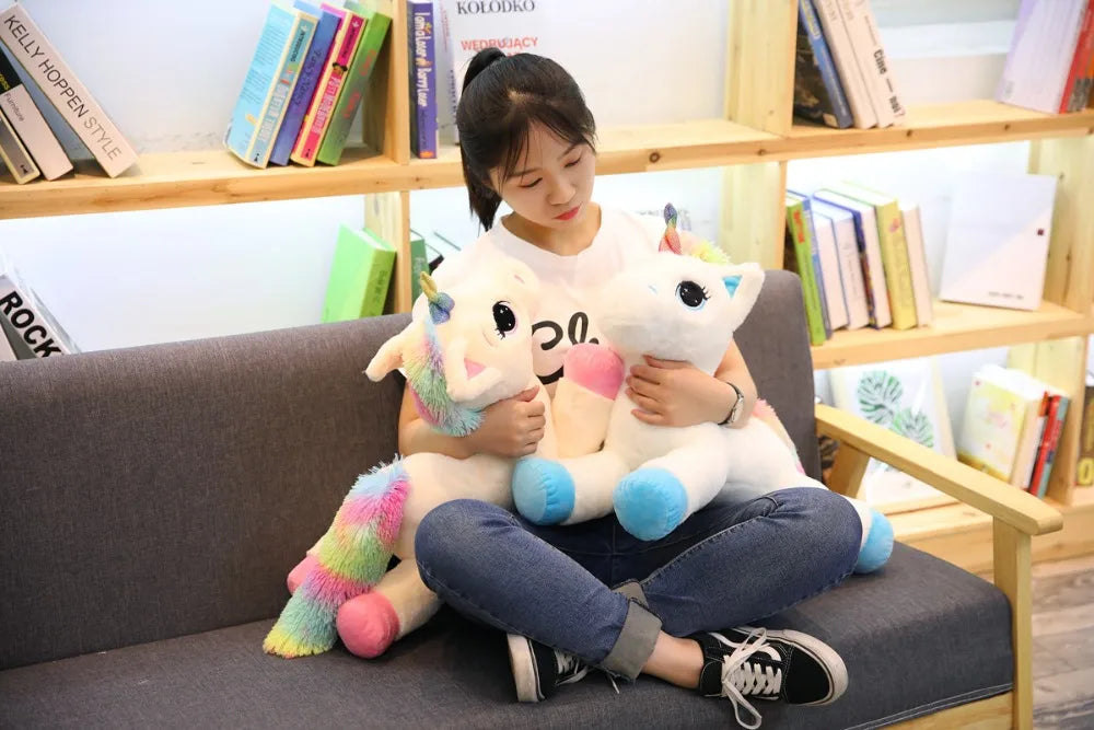 A young woman is sitting on a couch holding two white unicorn plush toys.