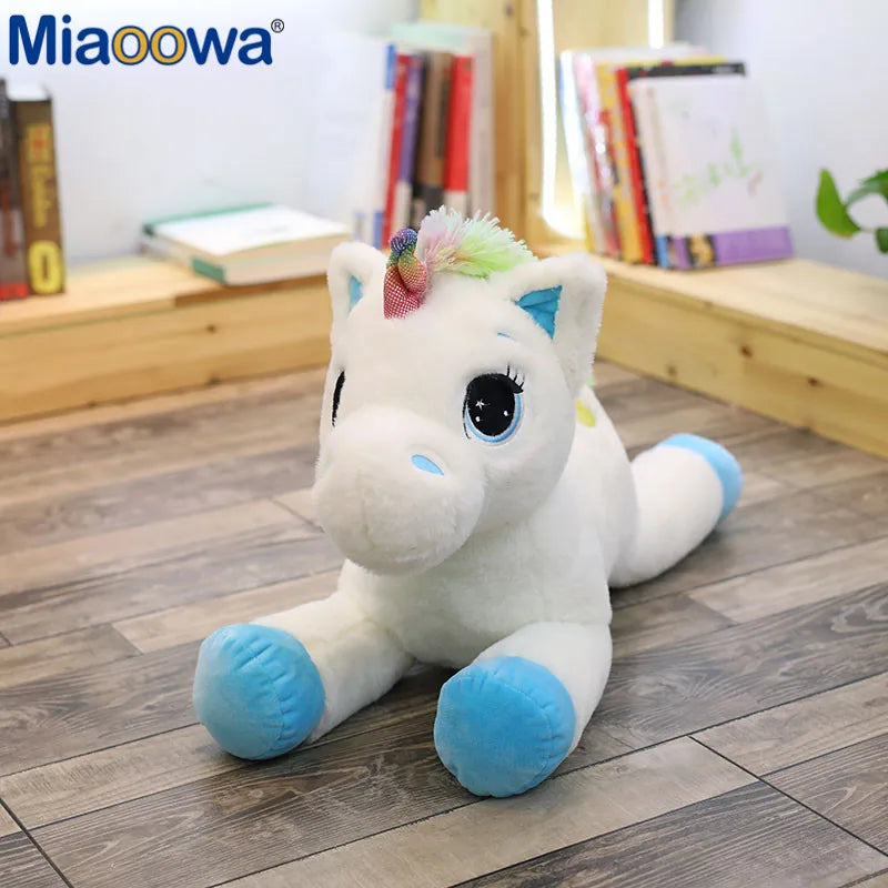 A white unicorn plush toy with blue accents and a colorful mane sitting on a wooden floor.