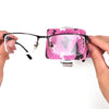 A hand holds a pair of black glasses with a pink camouflage printed elastic bandage tape attached to the frame.