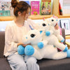 A woman is sitting on a couch holding several white unicorn plush toys.