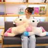 A young woman is sitting on a couch with two white unicorn plush toys.