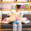 A young woman is sitting on a couch with two white unicorn plush toys.