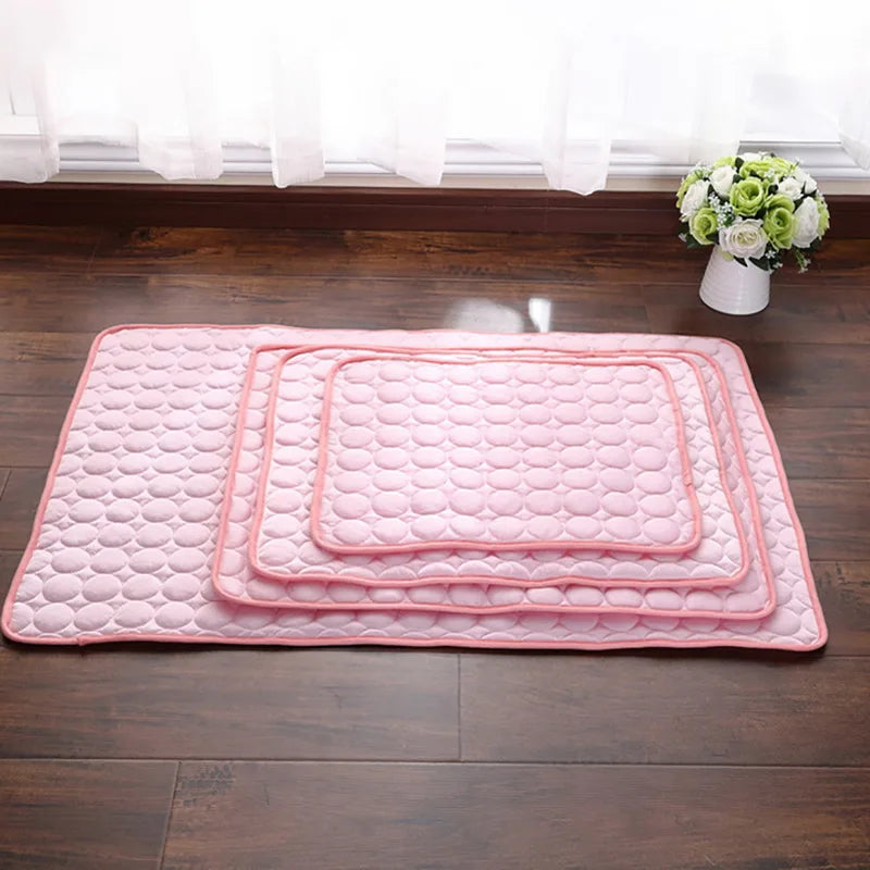 Pink quilted cooling pet mat for dogs and cats placed on a dark wooden floor near a window.