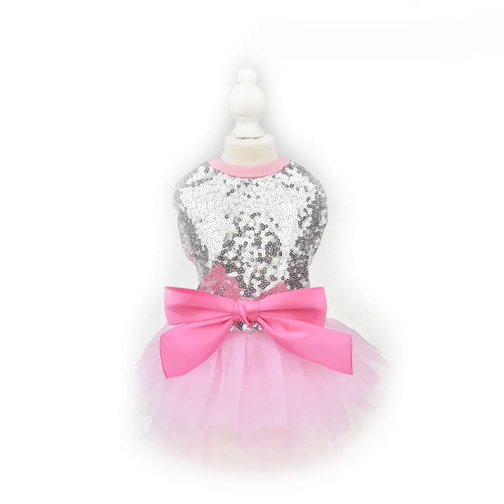 A pink sequined dog dress with a bodice and a large pink bow displayed on a white mannequin.