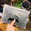 A hand holds a clear plastic bag containing black ink drawings of a duck swimming in wavy lines.