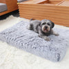 A fluffy gray dog bed is placed on a white rug in front of a wooden pet crate.