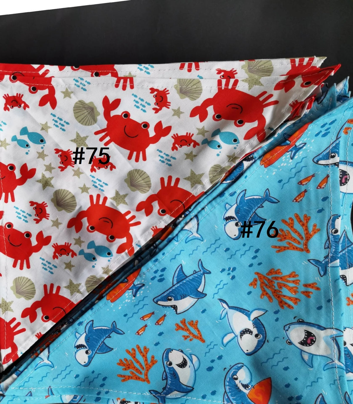 A close-up of colorful cotton pet bandanas featuring various animal designs and numbers 75 and 76