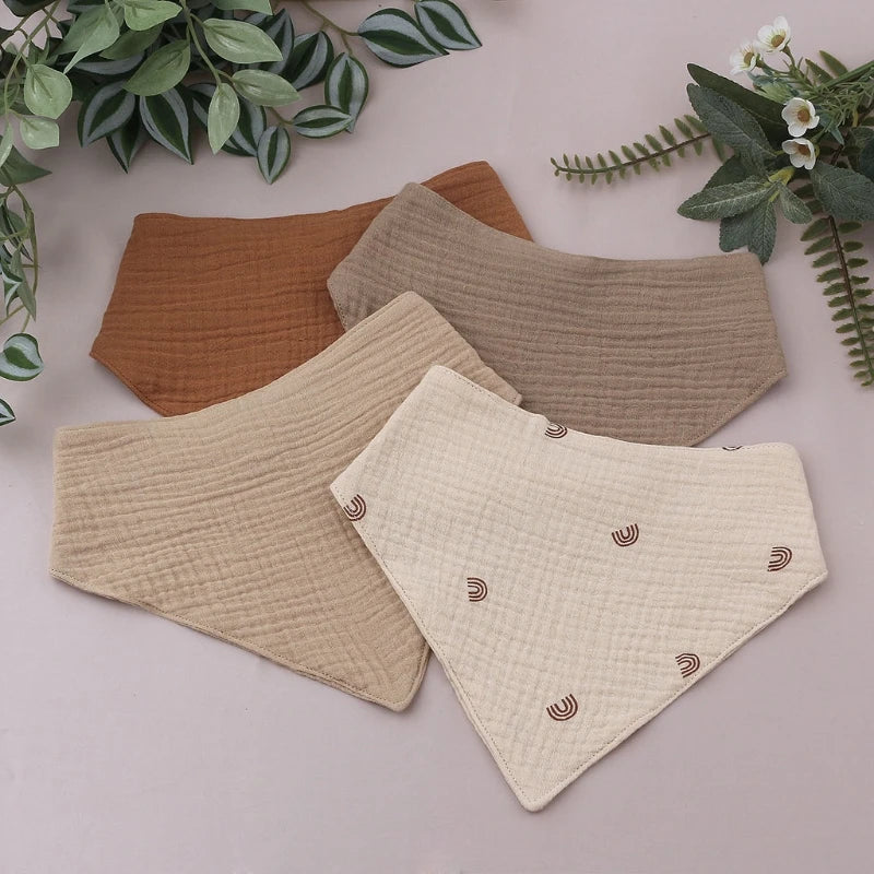 A set of three soft cotton baby bibs in brown and beige tones are displayed on a light surface.
