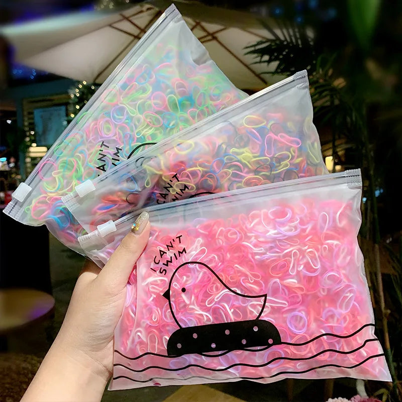 A hand holds a clear plastic bag filled with colorful elastic hair bands for girls.