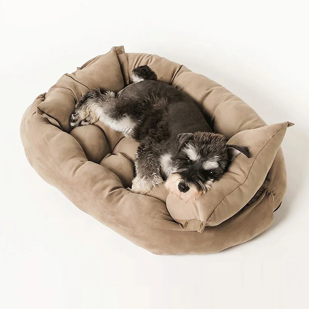 A fluffy black and white dog is resting inside a tan plush pet sofa bed with a raised rim.