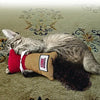 A tabby cat is lying on a carpet with a red KONG Kickeroo Cuddler Cat Toy.