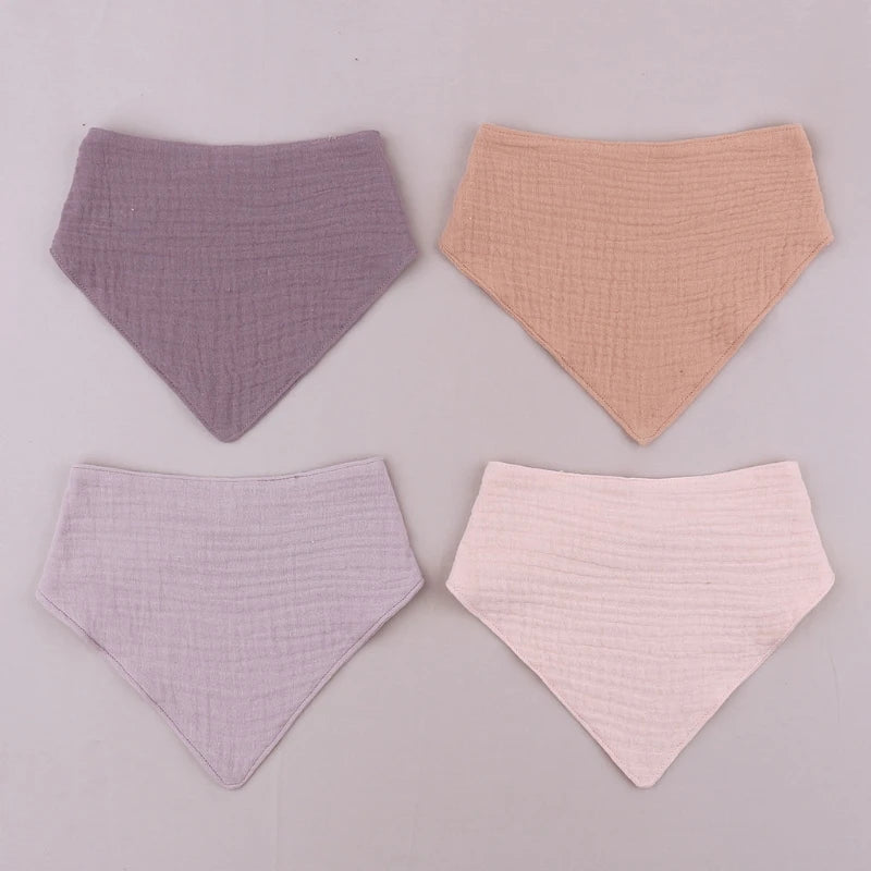 Three soft cotton baby bibs in lilac, peach, and pink shades displayed on a light gray background.