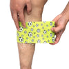 A hand is applying a yellow patterned self-adhesive elastic bandage tape to a person's leg.