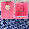 A pink rabbit hay and food rack with a wire grid and a circular opening sits on a blue grid surface.